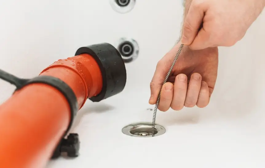 Plumber using drain snake to unclog bathtub