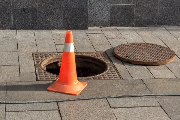 Emergency Sewer Repair Open sewer manhole cover and traffic cone on a city street